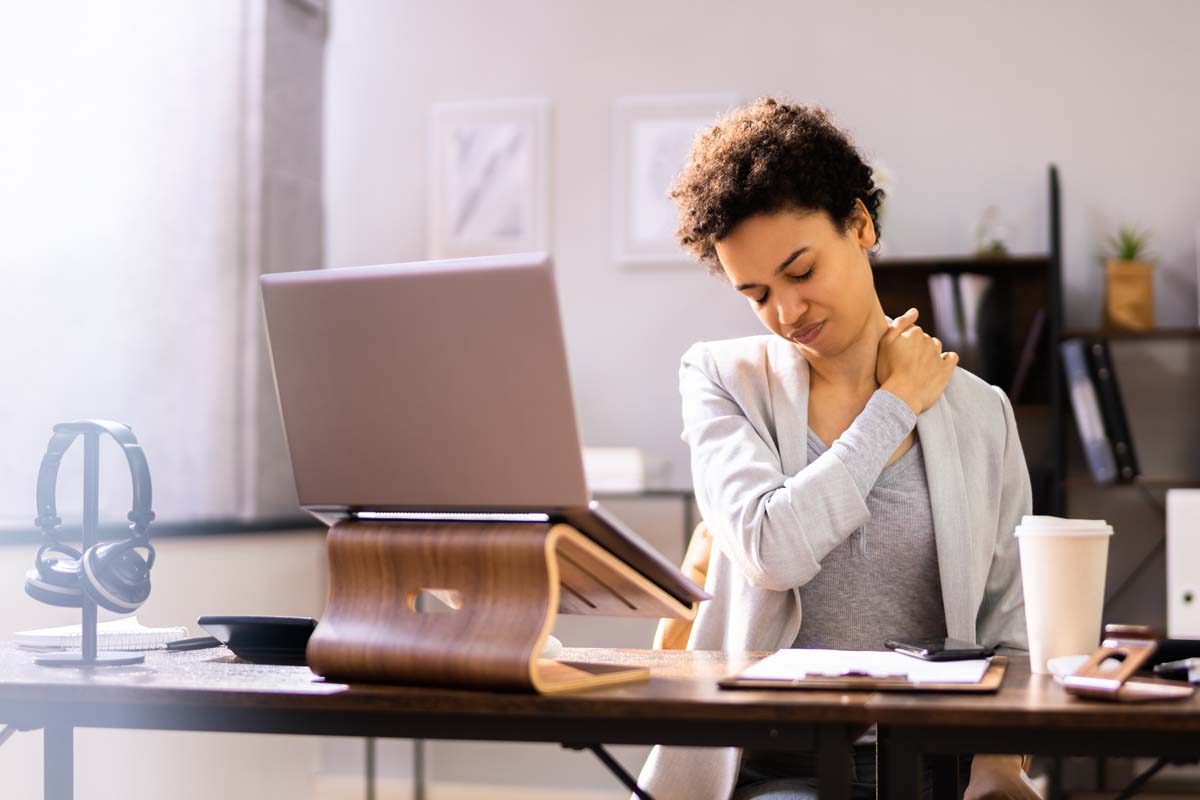 Frau mit Nackenschmerzen vor dem Schreibtisch.