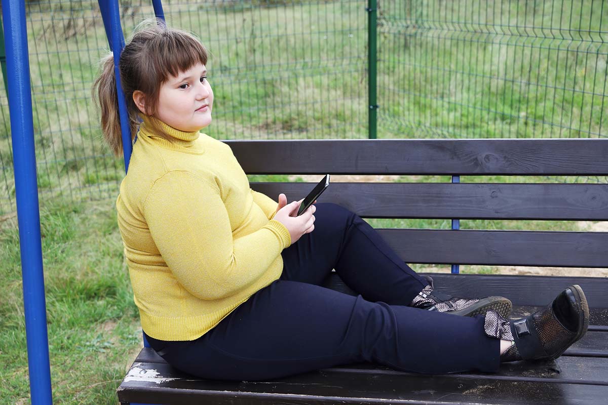 Übergewichtiges Kind sitzt auf Bank.